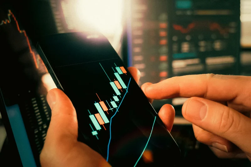 Investor monitoring stock trading charts on mobile phone for currency risk management and USD/THB hedging strategy for American expats in Thailand