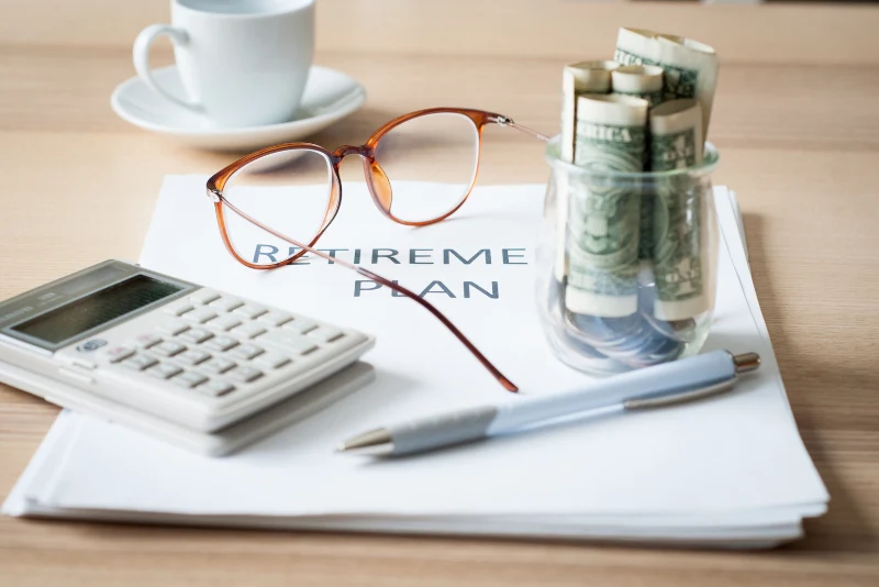 Retirement plan documents with rolled US dollar bills and calculator representing 401k and IRA management strategies for American expats abroad